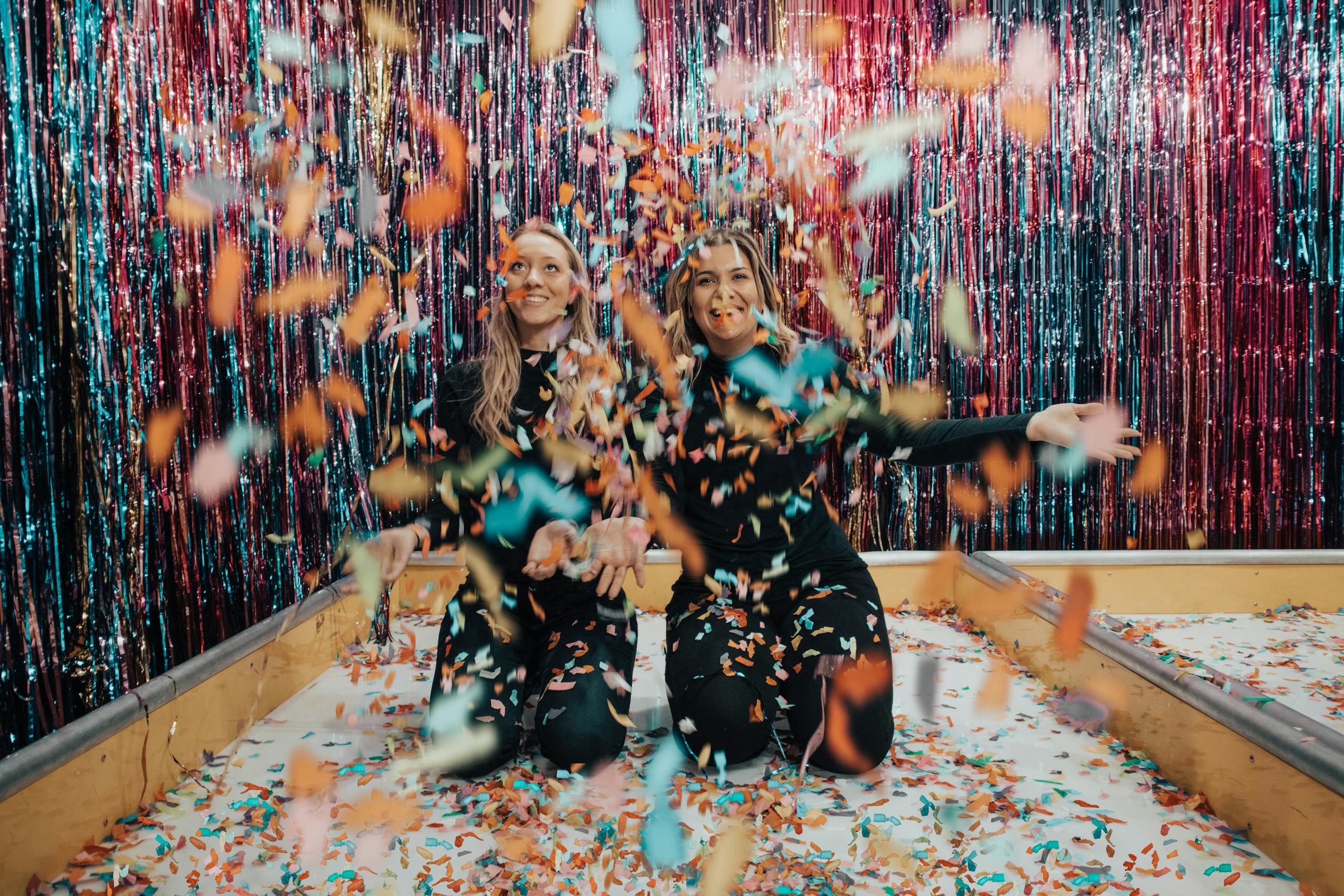 Two women enjoying a vibrant indoor celebration with colorful confetti.